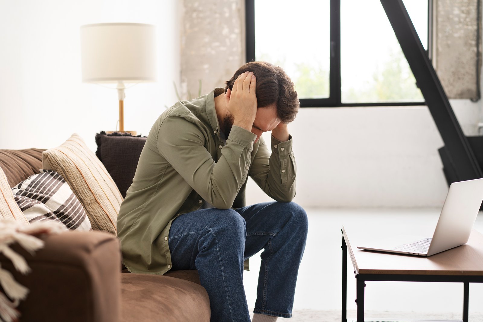 a man sitting with his head in his hands in front of a laptop, representing pressure and self-doubt around achievement
